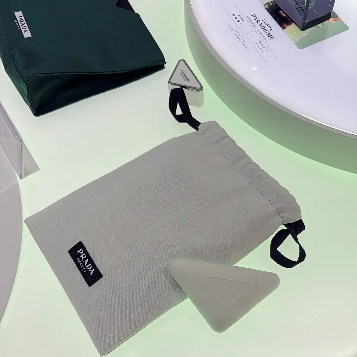 ニュウマン高輪　プラダ ビューティ ストア   購入額に応じてポーチのプレゼントなども実施中。この巾着型ポーチはニュウマン高輪限定だそう。ちなみに手前のトライアングル型のアイテムは10/8に全国発売予定の「プラダ ハンド トリプルケア ハンドクリーム」。この秋、大切な人や自分へのギフトにぴったりの“手の美容液”です。