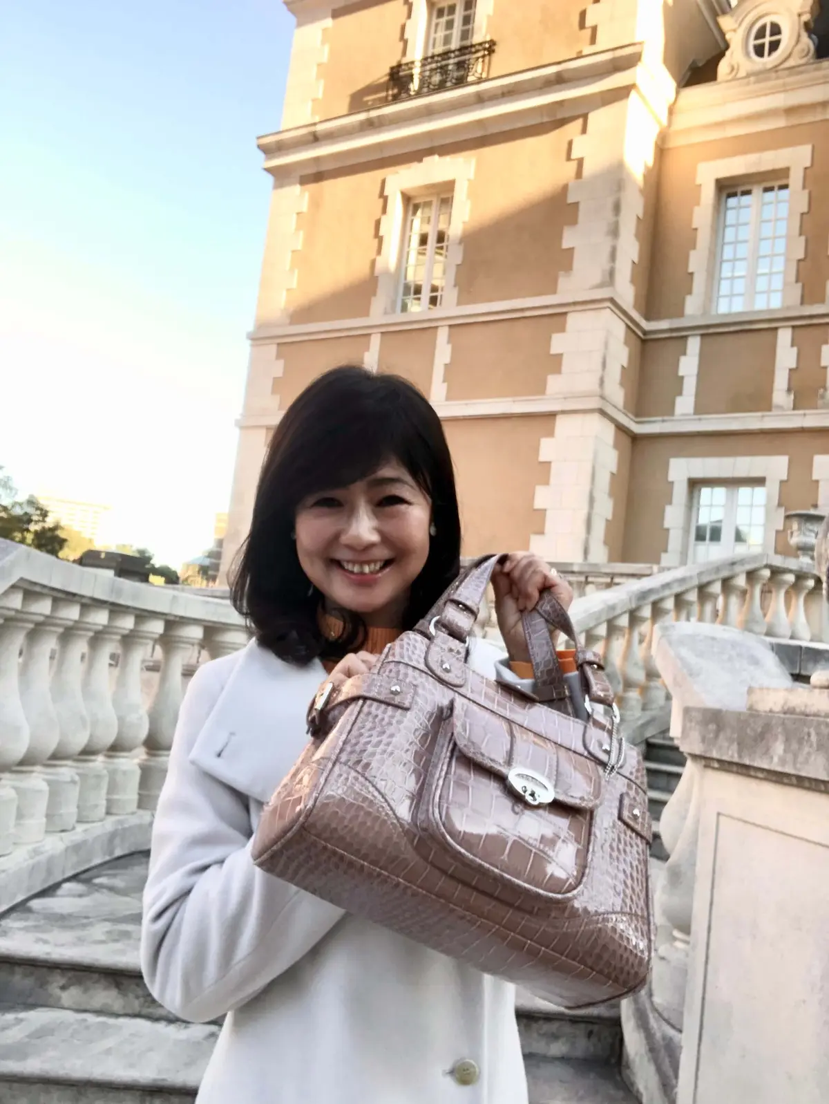 「ロペ」の白ロングコート。「リリーブラウン」のオレンジニット。ピンクベージュのクロコダイルバッグ。