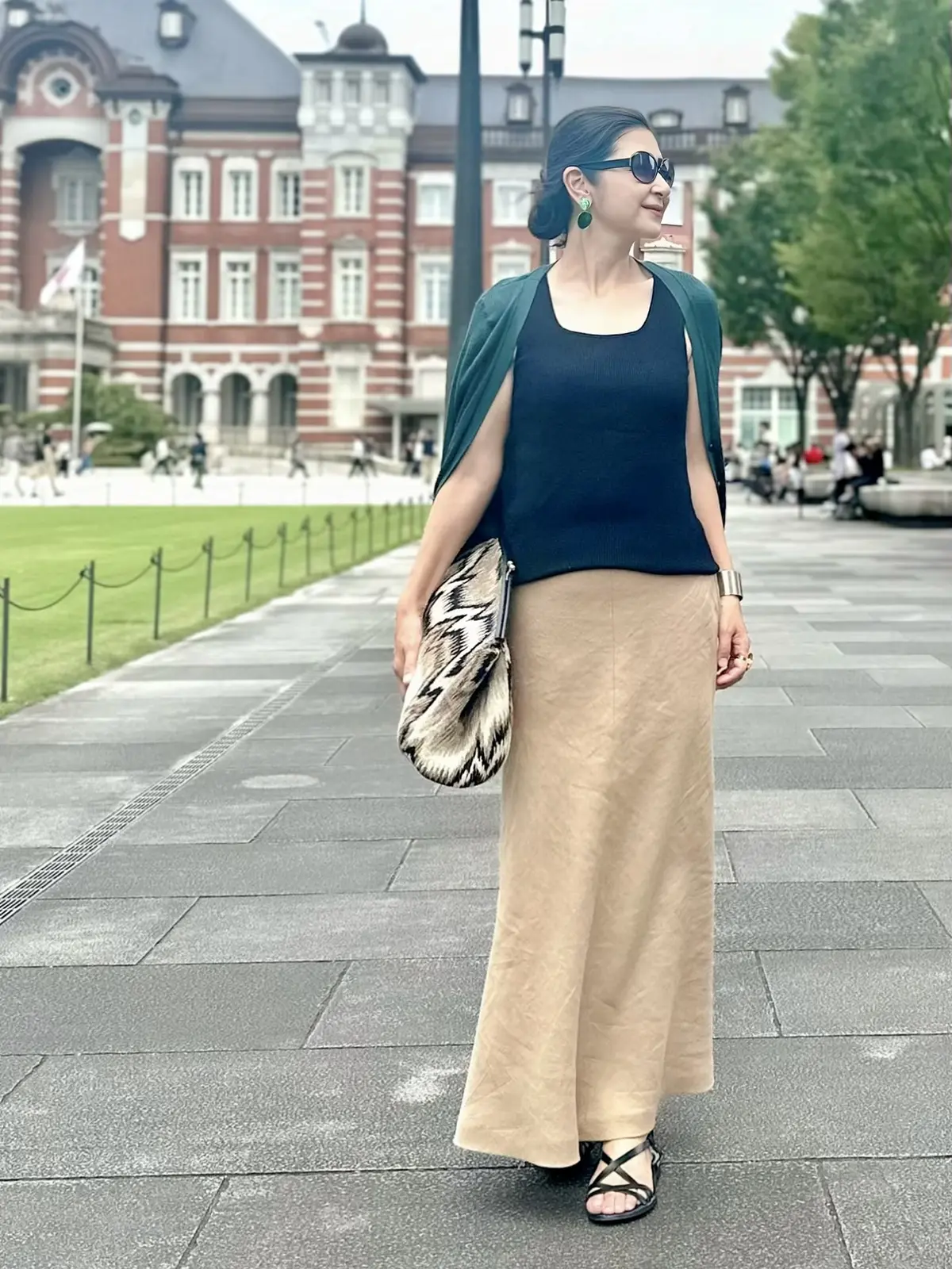 エクラプレミアムのキャメルの「リネンフレアスカート」黒のノースリーブニット、ダークグリーンのカーディガン、大きめクラッチバッグ、黒サンダル