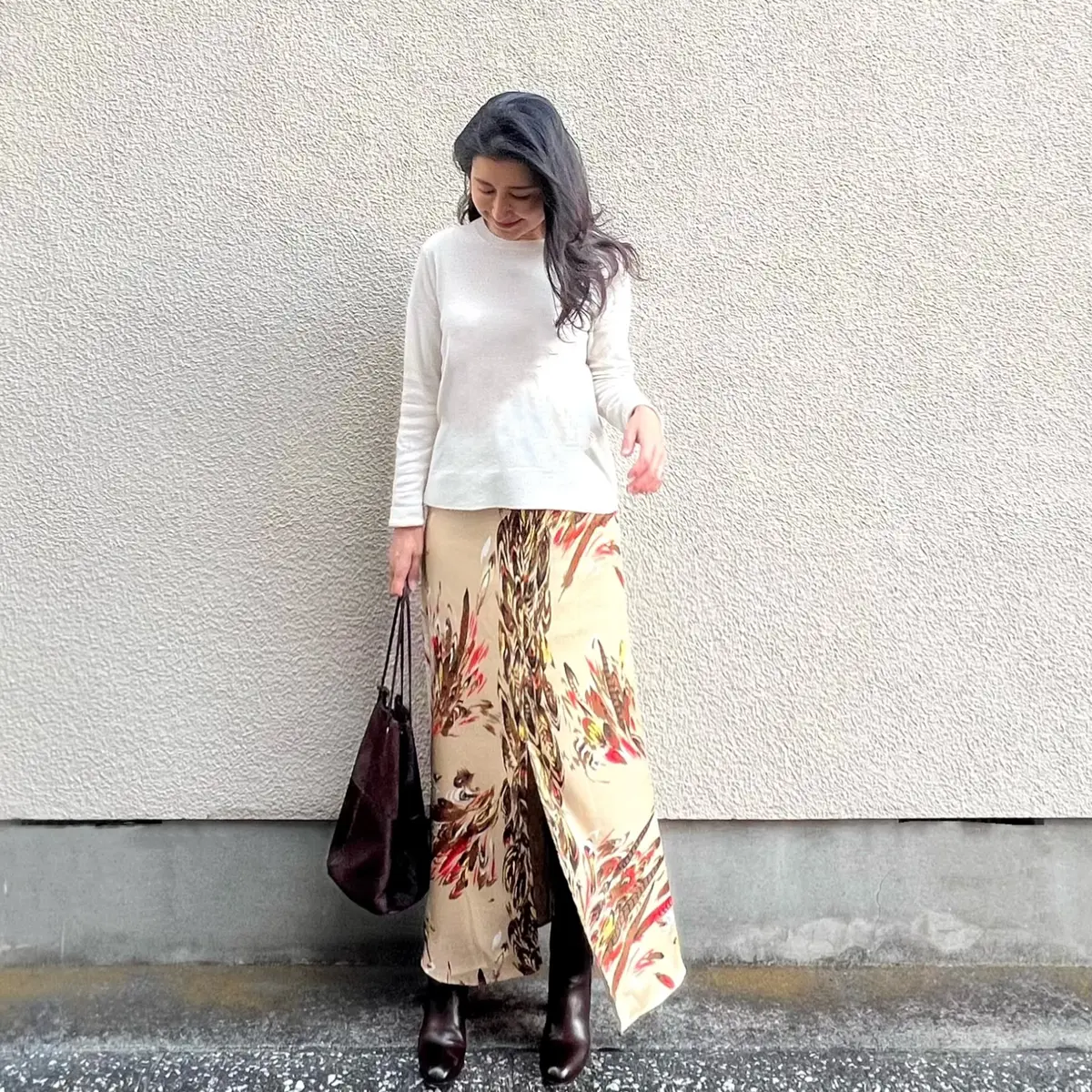 白のニット、ベージュの柄物スカート、ブラウンのバッグ、ブラウンのブーツ