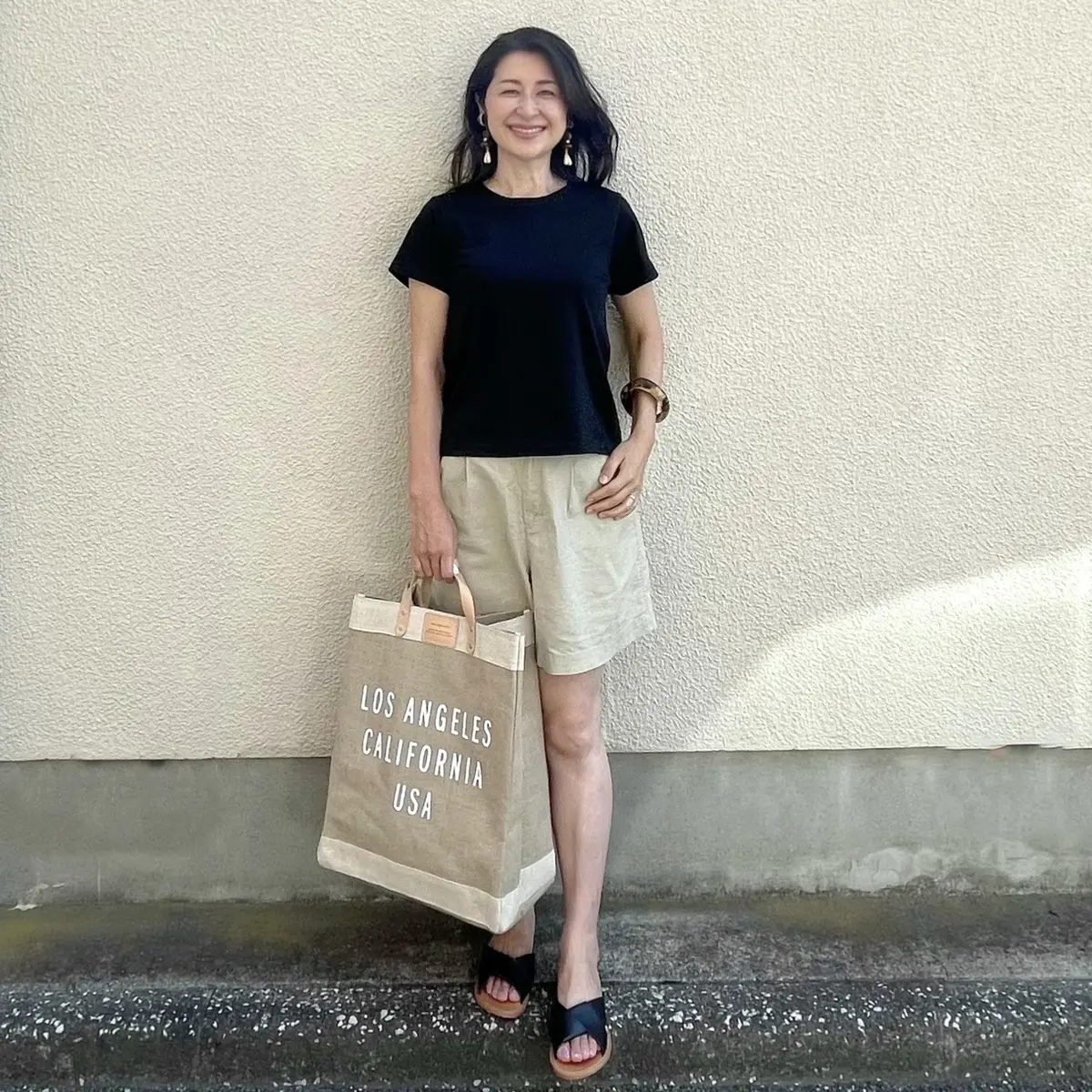 黒Tシャツ、ベージュのショートパンツ、黒サンダル、麻の大きめエコバッグ