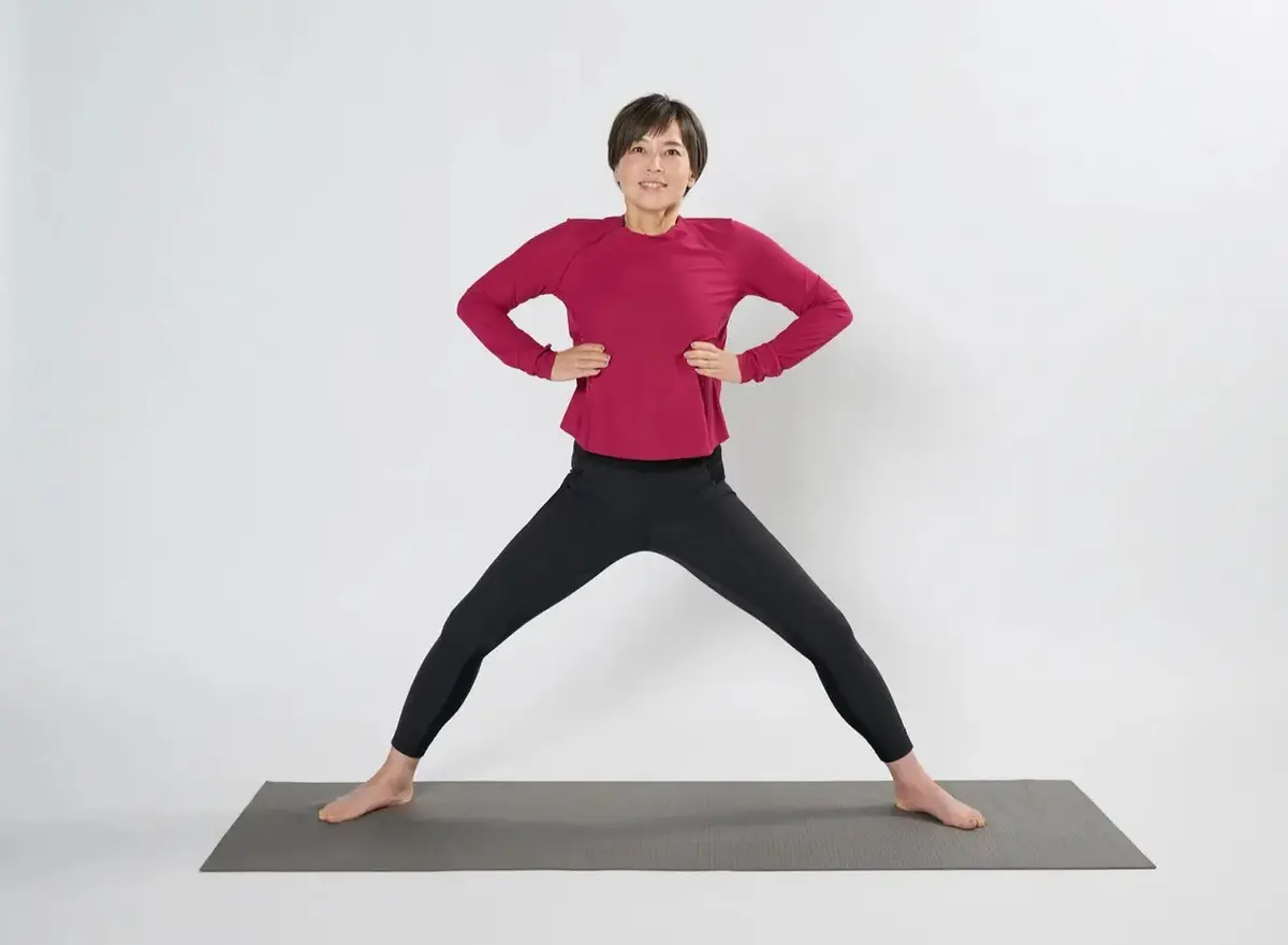 ①両脚を肩幅の1.5〜2倍ほど開いて立ち、つま先は45度程度、外に向ける。両膝を軽く曲げて、肋骨に両手を当て、骨盤はまっすぐに立てる。息を吸って、肋骨が360度膨らむようなイメージで大きく膨らませる。このときお腹は凹ませる。