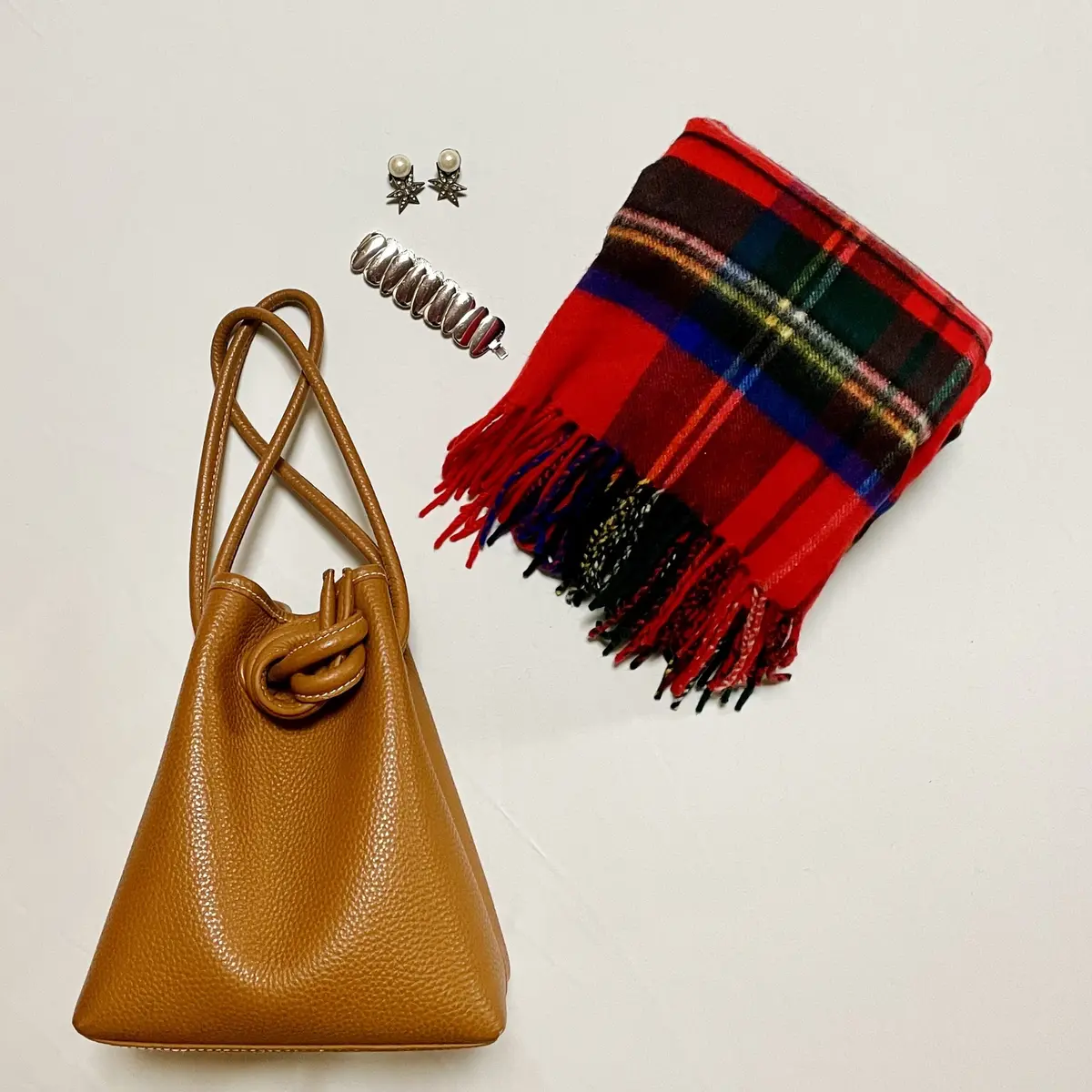 キャメルのバッグ、赤いチェックの大判ストール、パールと星形を組み合わせたイヤリング、シルバーの太めブレスレット