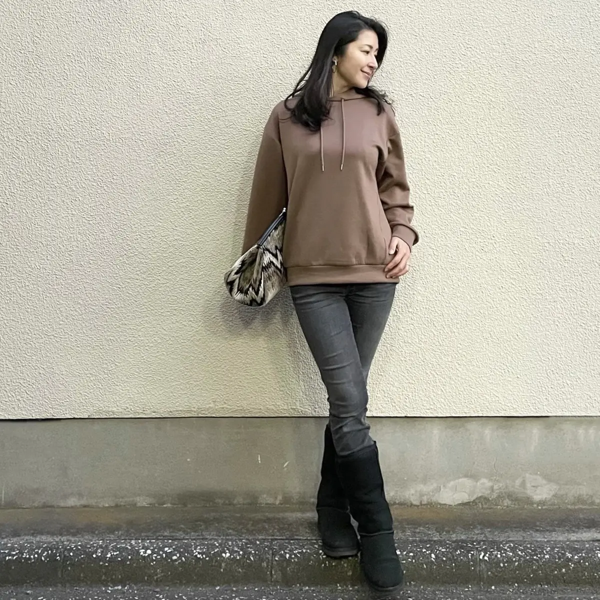 オレンジ系ブラウンのパーカー、ブラックデニム、ムートンブーツ、大きめクラッチバッグ