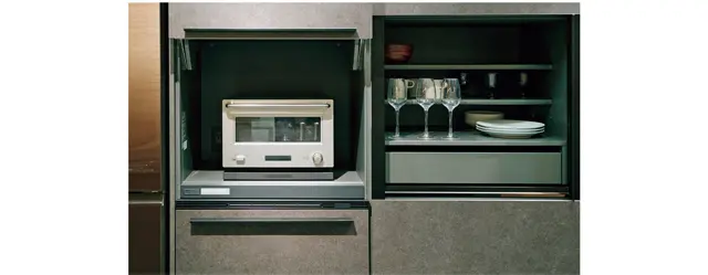 人気のグレー系のアイランドキッチン。背面収納も充実し、左のキッチン家電用の棚は扉を閉めると電源が切れる。その下は炊飯器用収納で、蒸気処理ができるため閉めたままで炊飯可能