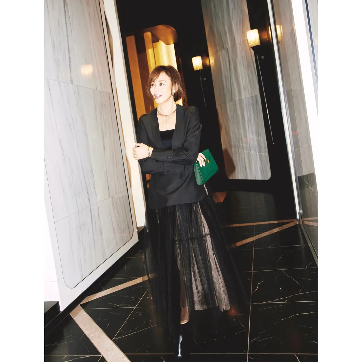 黒Vネックブラウスに黒オーガンジースカートを合わせ、グリーンのクラッチバッグを持ったコーディネート　モデル・SHIHO　