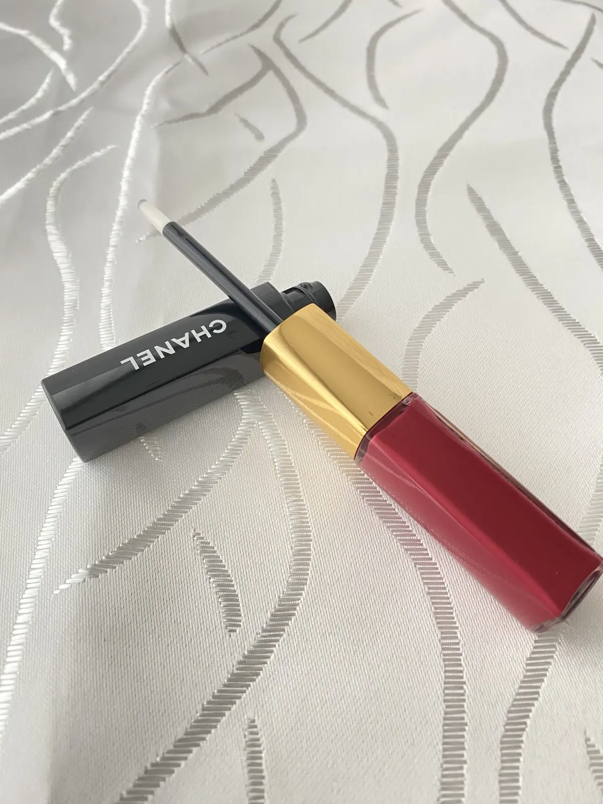 CHANELのルージュ デュオ ウルトラ トゥニュ、ゴールドキャップとクリアトップコートのリップグロスが開いた状態の写真