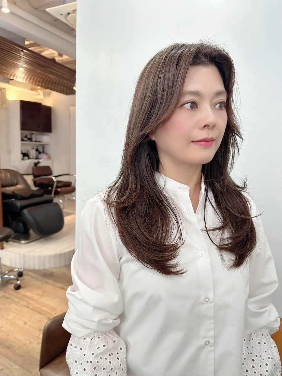 原宿「ハーツ」の店内にいるロングヘアの女性。顔まわりに動きを持たせたロングヘアスタイルの女性。白いブラウスが上品な印象を添えて、春らしい軽やかさを感じる一枚。。