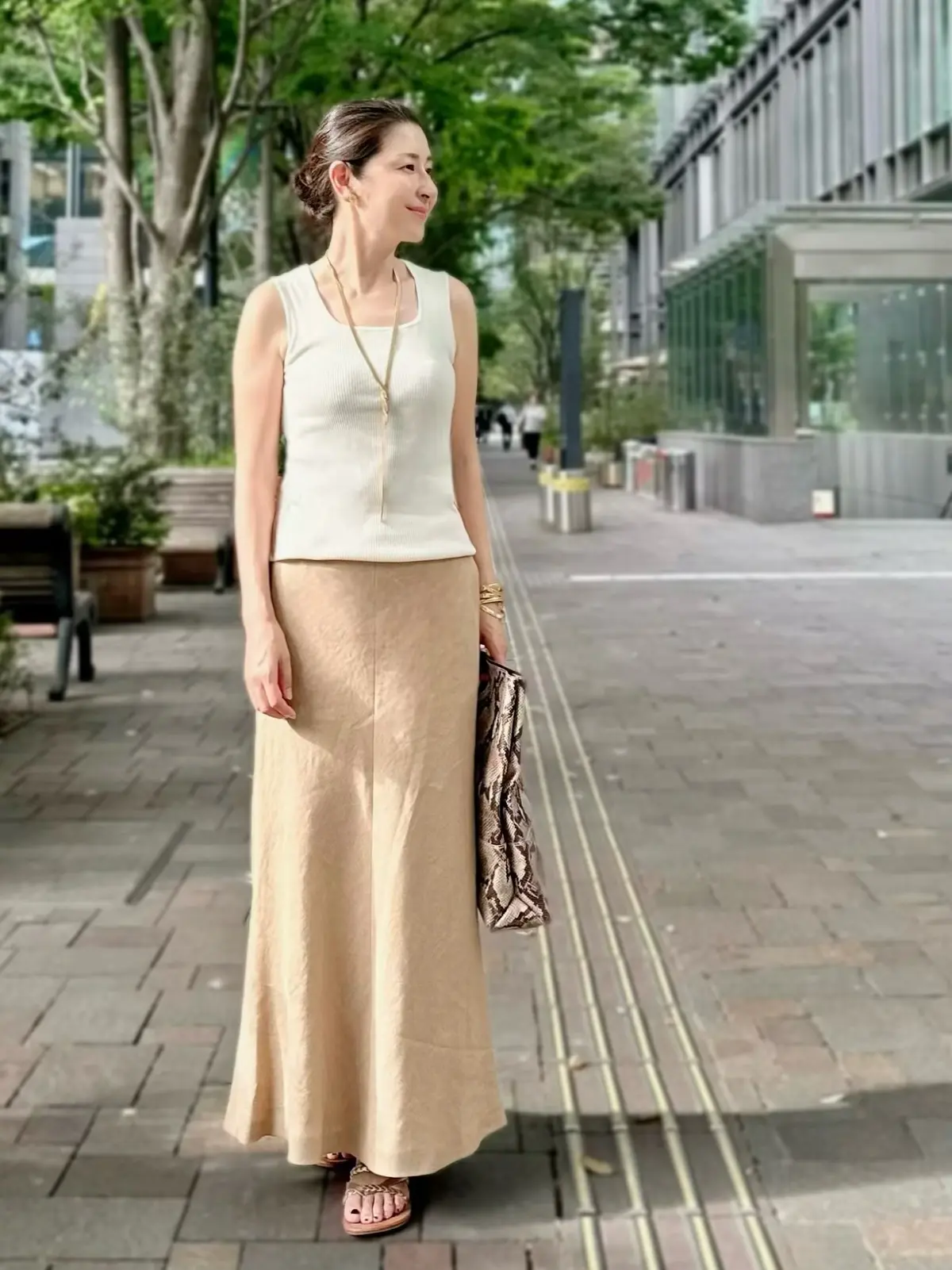 エクラプレミアムのキャメル「リネンフレアスカート」、白ニット、パイゾン柄バッグ、ゴールドのフラットサンダル
