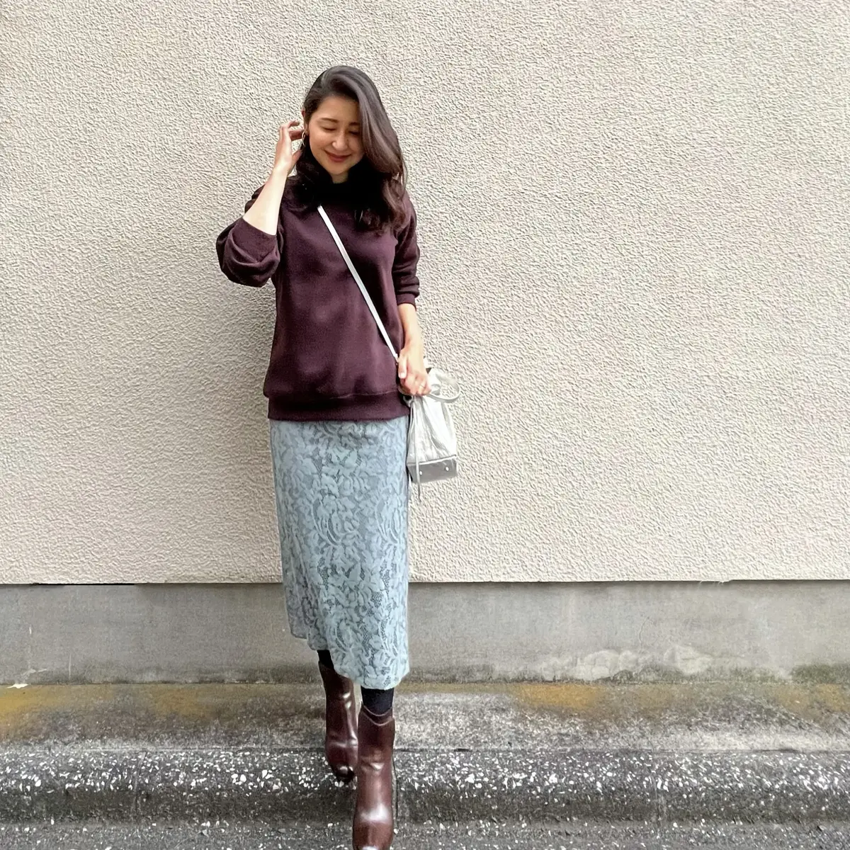 ブルーグリーンのレースタイトスカート、ブラウンのスウェット、シルバーのポシェット、ブラウンのブーツ