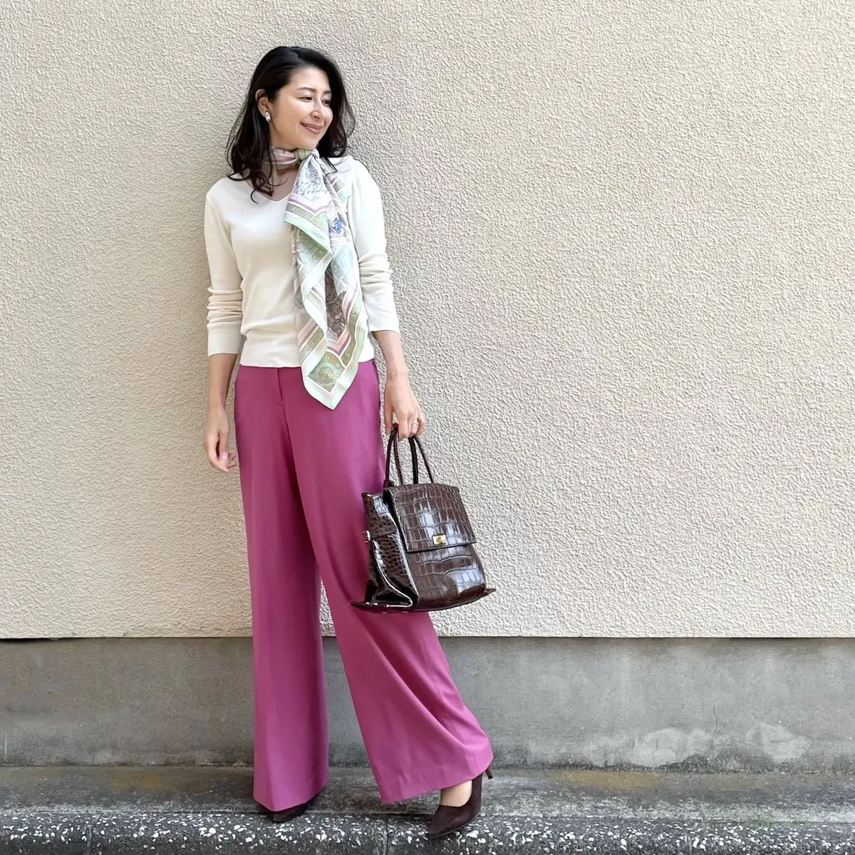 白のVネックニット、ピンクのワイドパンツ、スカーフ、ブラウンのバッグとパンプス