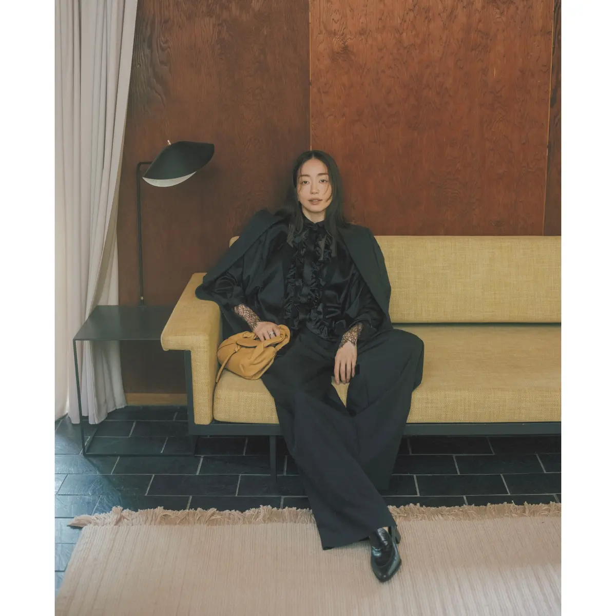 黒フリルつきサテンブラウスに黒ジャケットとパンツを合わせたコーディネート　モデル・松島花