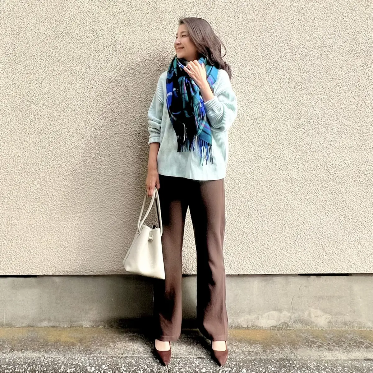 茶ニットパンツ、水色ローゲージニット、ブルー系の大判チェック柄ストール、白バッグ