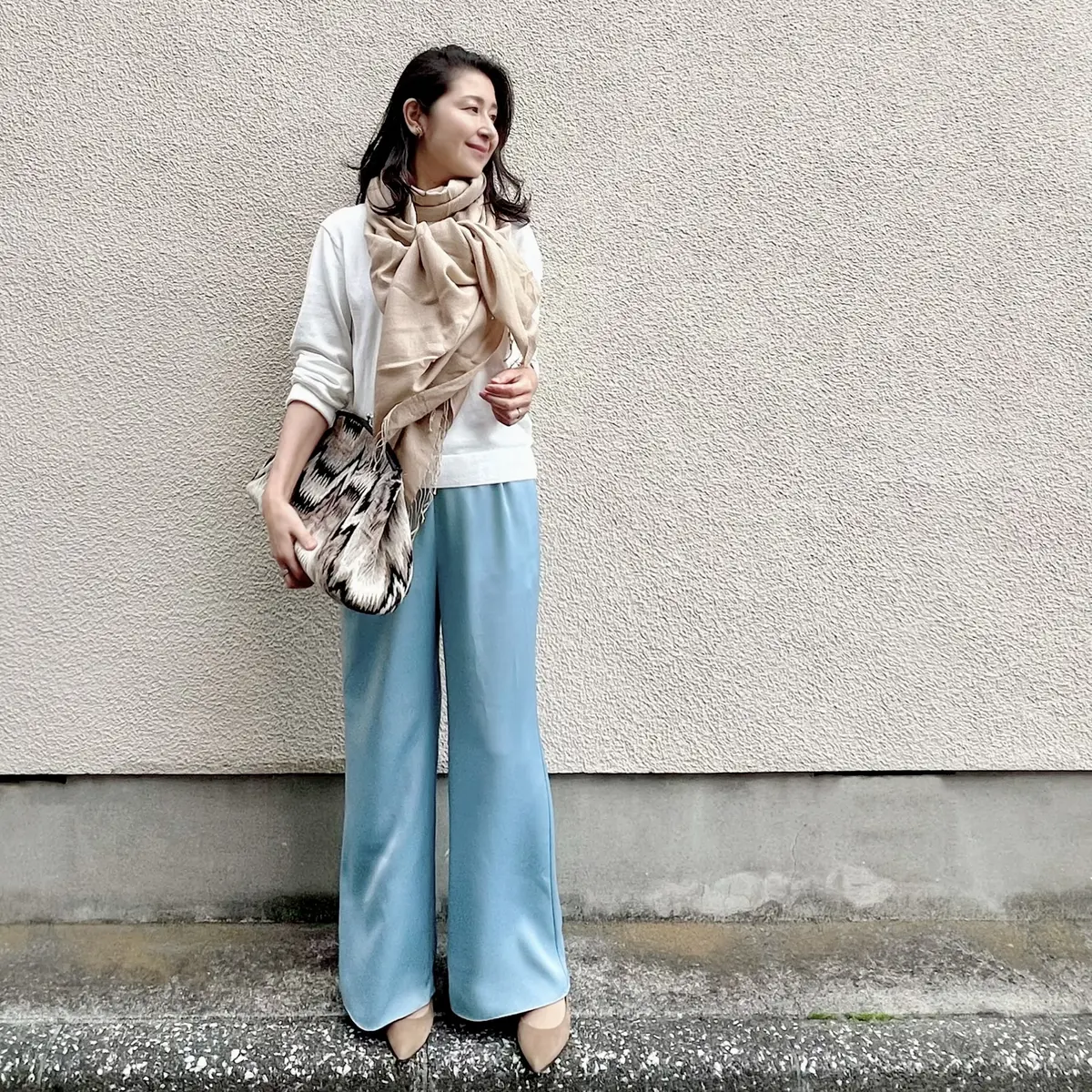 白ニット、ライトブルーのパンツ、ベージュのパシュミナストール　柄物大ききめクラッチバッグ　ベージュのパンプス