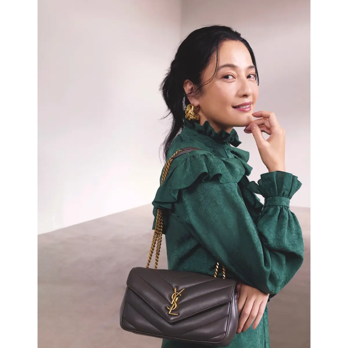 首元と袖口、肩周りにフリルをあしらったグリーンのブラウスに、ゴールドチェーンストラップがついたグレーバッグを合わせたコーディネート　モデル・熊沢千絵