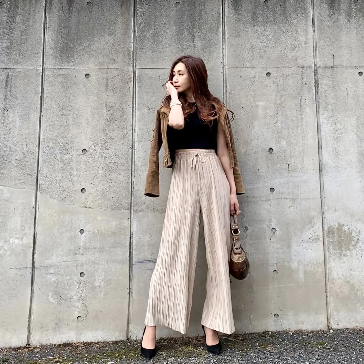 ベージュのライダースジャケット、ブラックのショートトップス、ベージュのワイドパンツ