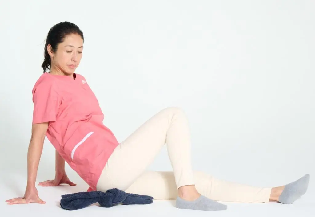 OurAge×Webエクラ　②床に座って、左脚を真っすぐに伸ばします。右の坐骨の下にタオルの結び目がくるように置いて、坐骨に体重をかけて結び目をゴロゴロと転がし、坐骨まわりをよくほぐしましょう。反対側も同様に行います。テニスボールやフォームローラーなどを使ってほぐしてもOK。