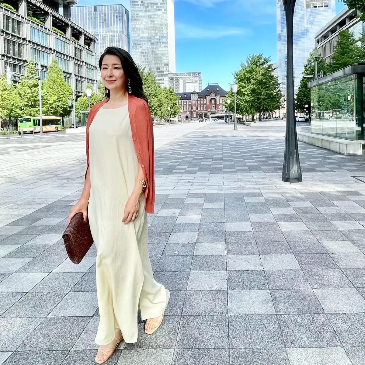 アイボリーのロングワンピース、ダークオレンジのカーディガン、ラフィアのクラッチバッグ、ベージュ系サンダル