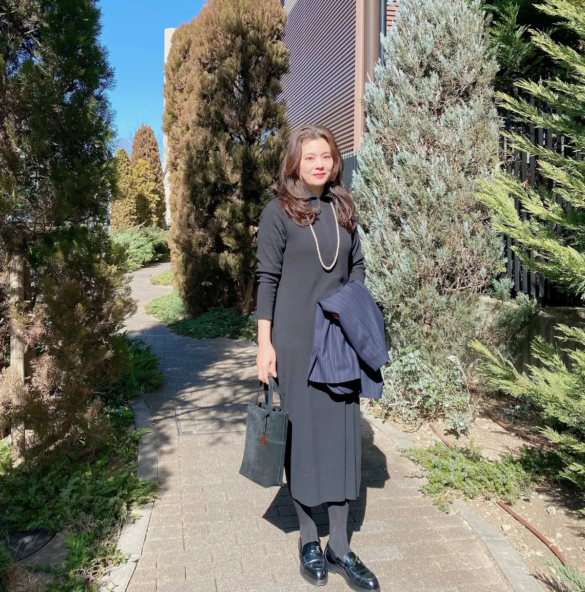 黒のユニクロハーフジップニットワンピースを着てパールのロングネックレス、ジャケットとグッチのバッグを持った女性の写真