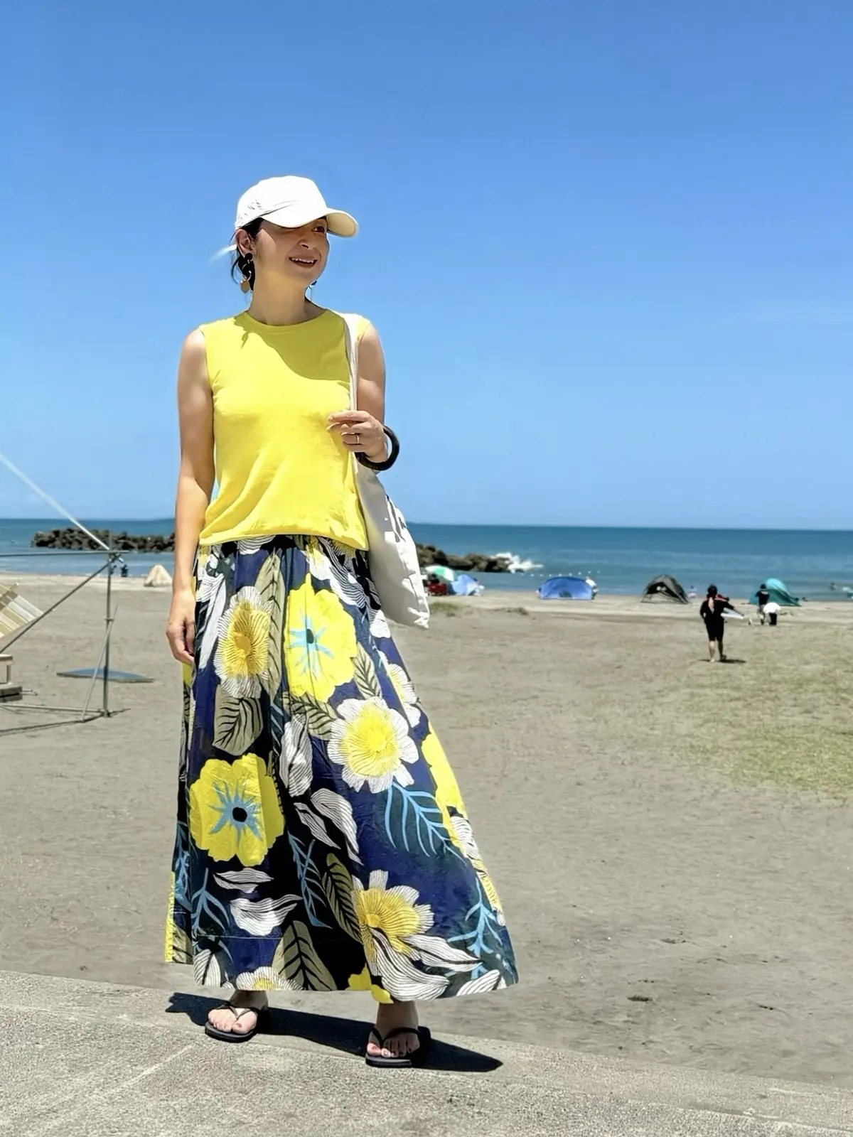 黄色のニット　花柄スカート　ビーチサンダル　ベージュのトートバッグ　ベージュのキャップ
