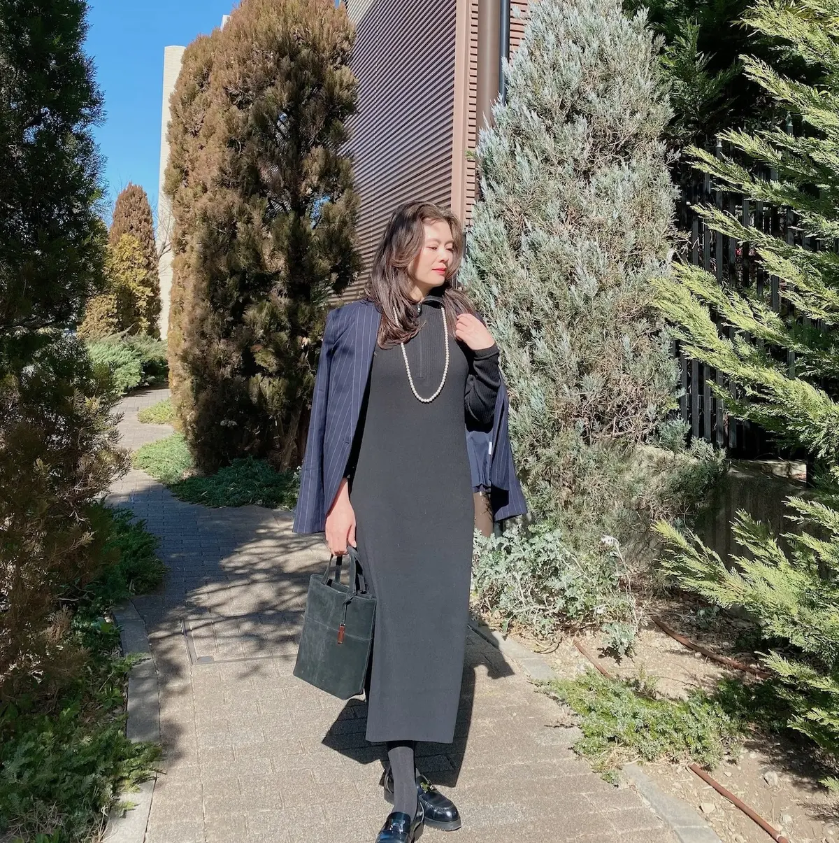 ユニクロハーフジップニットワンピースを着てパールのロングネックレス、ジャケットを羽織り横を向いた女性の写真