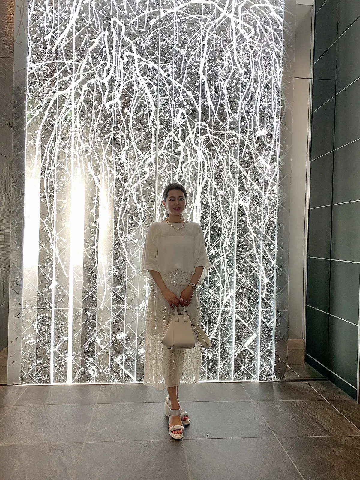 白の異素材を重ねた大人のホテルランチコーデ 光の前に立つ女性