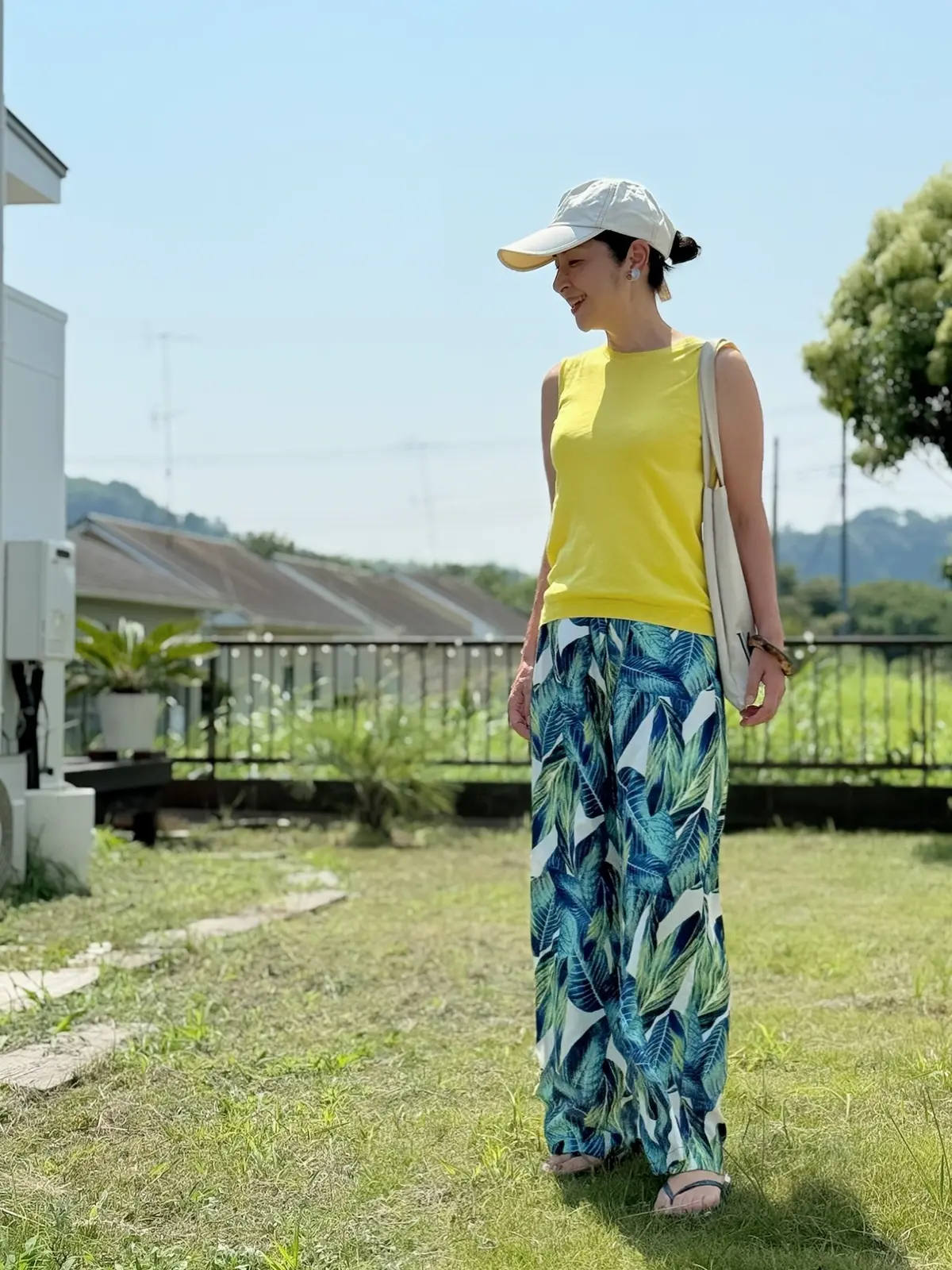 黄色のノースリーブニット　リーフ柄のワイドパンツ　ベージュのトートバッグ　ビーチサンダル　ベージュのキャップ