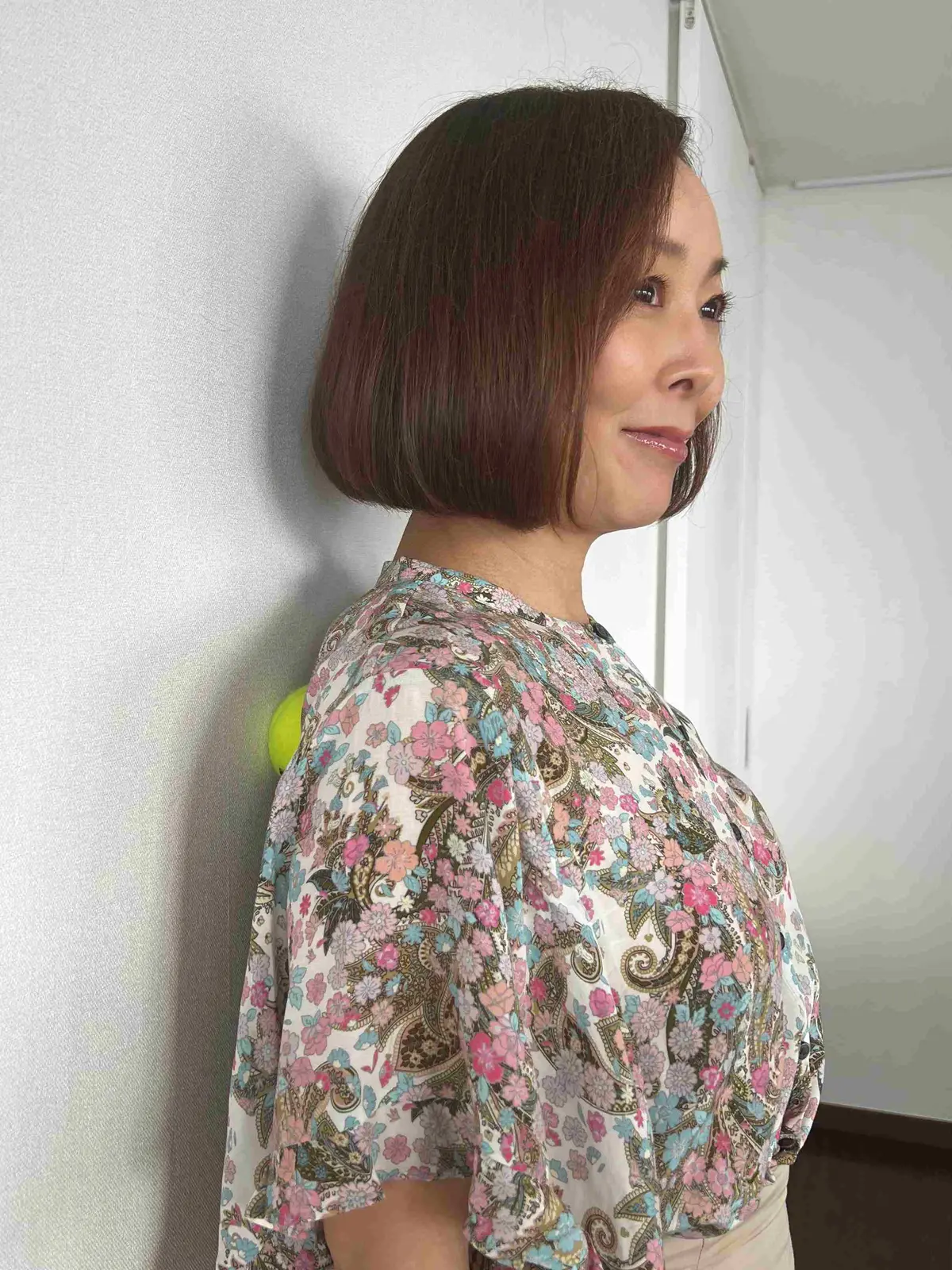 壁の前に立ち、壁と背中のあいだにテニスボールをはさむ。背中を動かし、肩甲骨まわりの筋肉をほぐすようにボールを転がす。