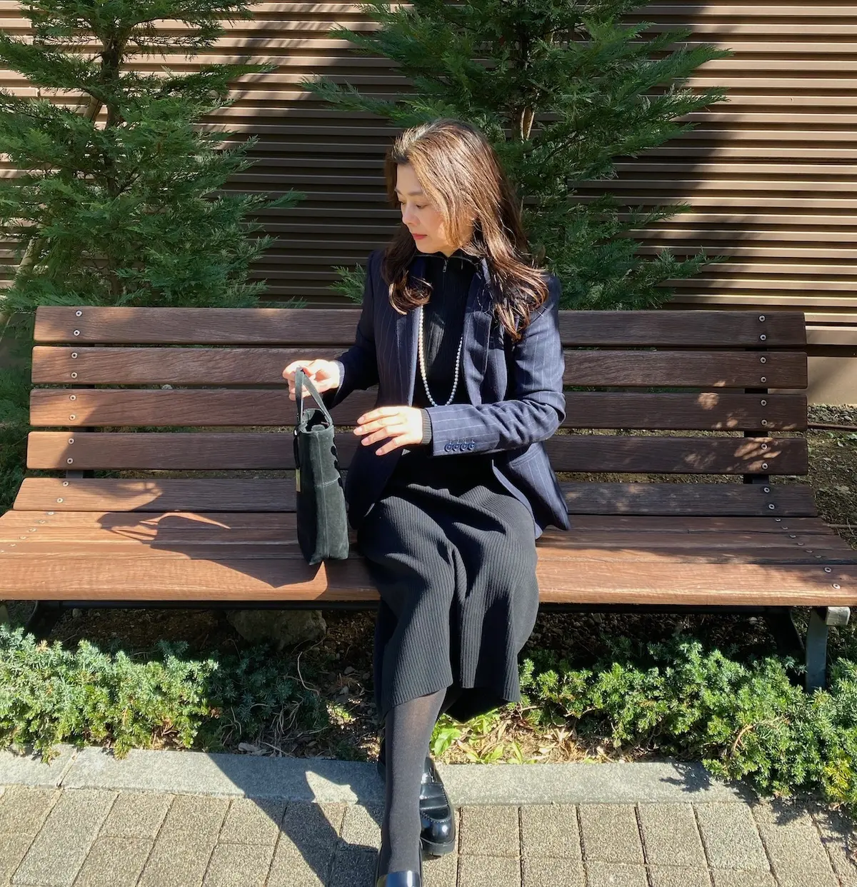 ユニクロハーフジップニットワンピースを着てパールのロングネックレス、ジャケットを羽織り横を向いた女性の写真