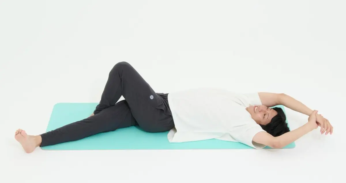 OurAge×Webエクラ　2)　右手を上げ、左手でつかみます。背骨を横に倒していくイメージで、上げたほうの手とともに上体を横に曲げていきます。呼吸を止めないように、左右各30秒ほど行って。