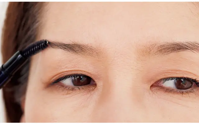 スクリューブラシで、低いほうの右眉は上側に、高いほうの左眉は下側にとかして毛流れ自体も左右、近づけるように整えておく。