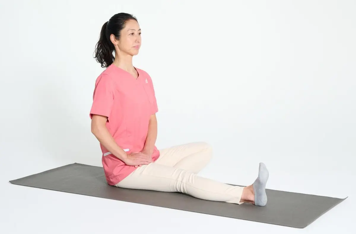 OurAge×Webエクラ　①床に座って右脚を真っすぐ伸ばして足首を直角に曲げ、左脚は内側に曲げます。両手を股関節のあたりに当てます。背すじは真っすぐに伸ばしましょう。