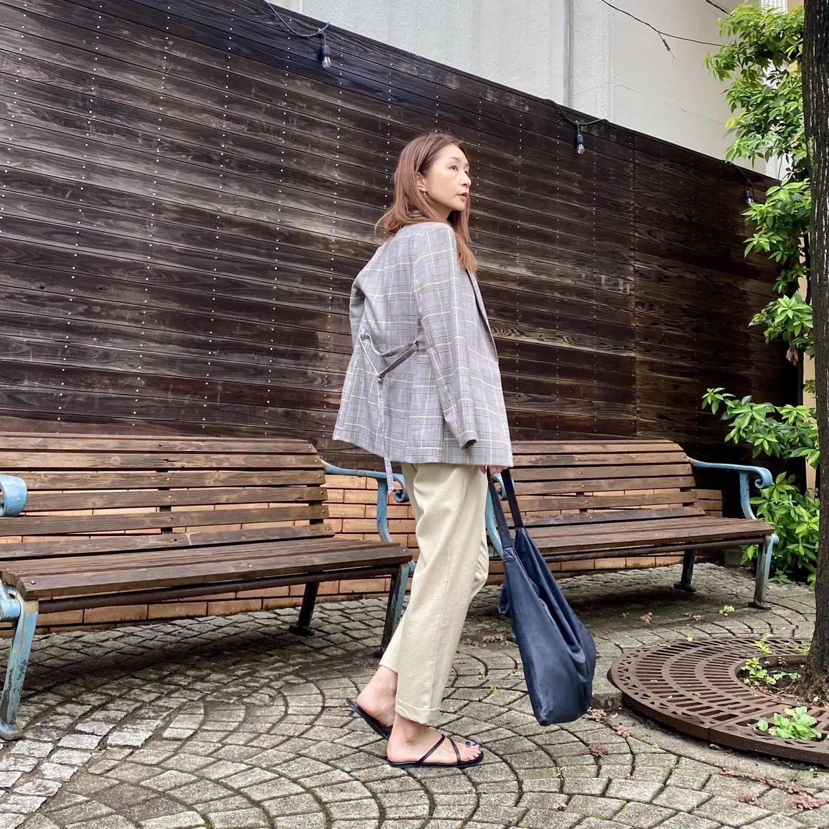 お尻が隠れるくらいの長めな千鳥柄のジャケットを羽織って黒サンダルとバッグを持ってます