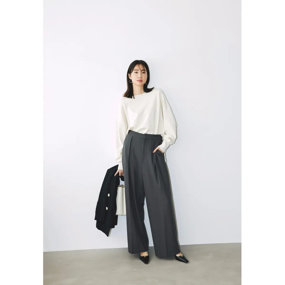 白ブラウスにダークグレーのタックワイドパンツを合わせ、ネイビーブレザーと白バッグを手に持ったコーディネート　モデル・絵美里