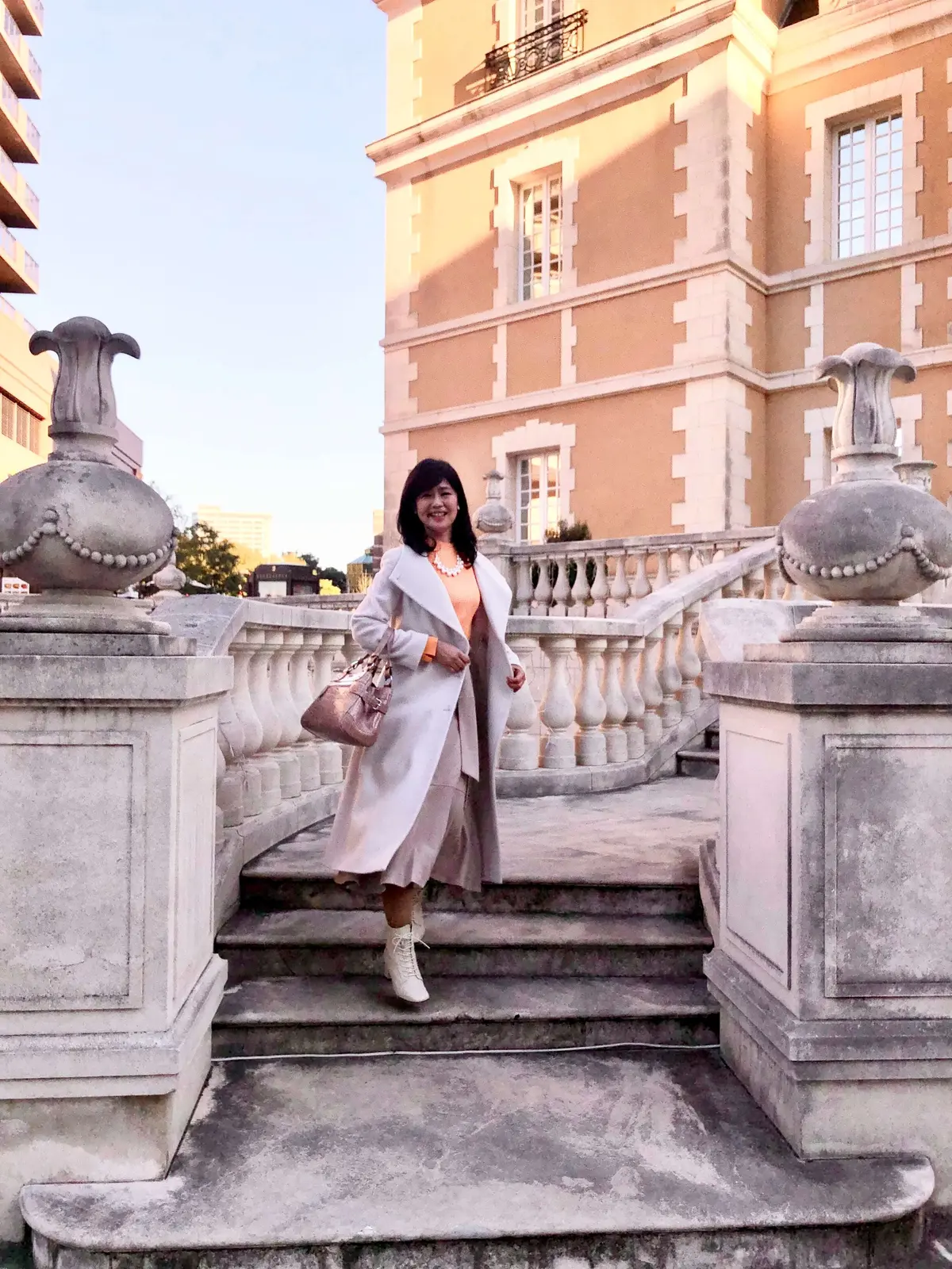 「ロペ」の白ロングコート。「リリーブラウン」のオレンジニット。「プールスタジオ アリヴィエ」の大振りパールネックレス。「ジェリービーンズ」の白ショートブーツ。