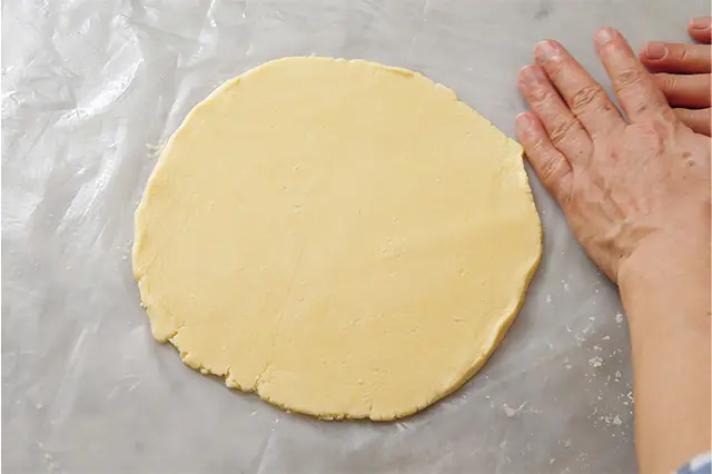 円形になるように生地の周囲を 寄せながら型より3～4㎝大き くなるようにのばす。