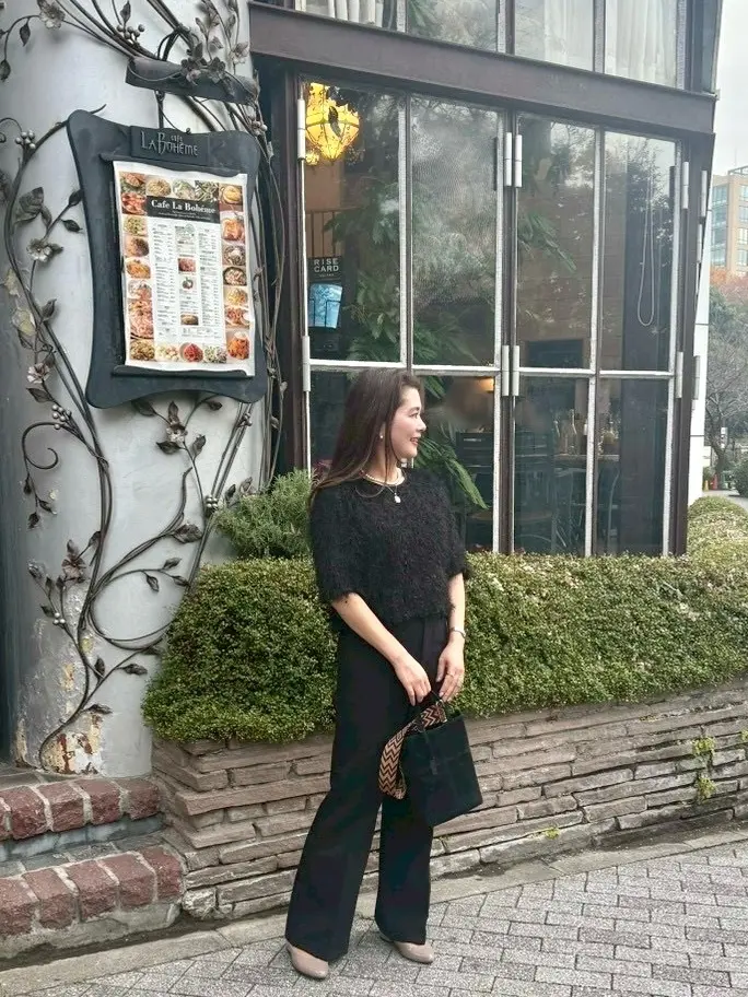 ユニクロスマートフレアパンツの丈長めを着用した50代女性のきれいめコーデ。新宿御苑ラ・ボエム前で横向きに立つ全身ショット。ヒール合わせで脚長効果のあるフレアパンツ。