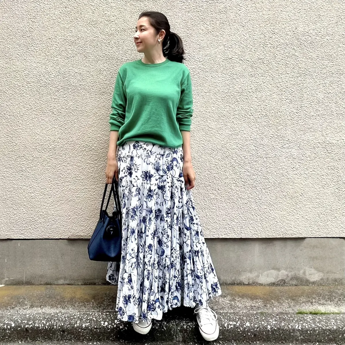 ユニクログリーンのニット、白にネイビーで花柄が描かれたロングフレアースカート、白のスニーカー、ネイビーのバッグ