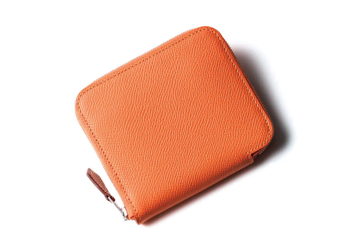 太陽のようなオレンジをまとった上質レザーと対照的に、中身はエキゾチックなシルクのライニング。がらりと表情が変わるのも 魅力。薄手のボディがエレガントな印象を授ける。小銭入れ1、カード挿し8。二つ折りウォレット（9.5×11.5）￥185,900／エルメ スジャポン（エルメス）