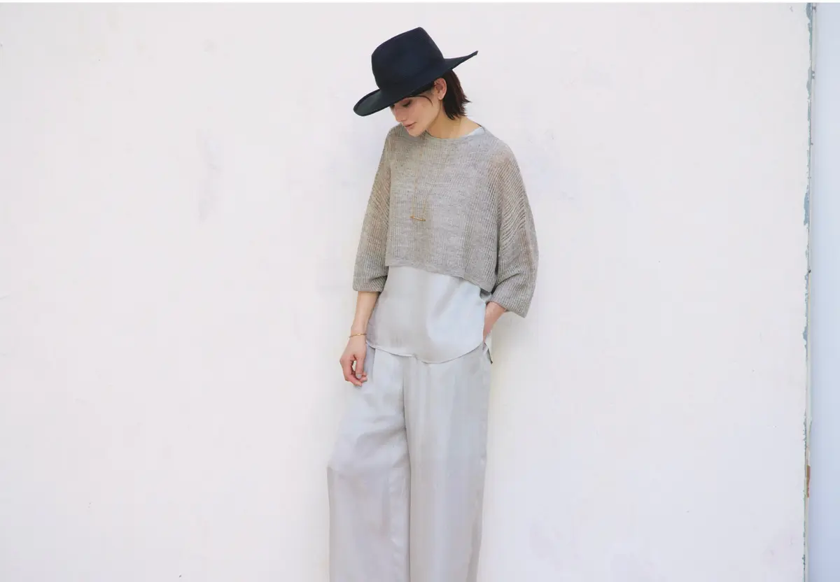 グレーシアーニットとライトグレーのサテンタンクトップの重ね着にライトグレーパンツを合わせて、黒ハットをかぶったコーディネート　モデル・渡辺佳子