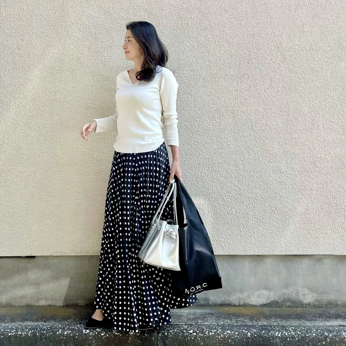 白のVネックハイゲージニット、黒ベースのドット柄ロングフレアスカート、シルバーのバッグ、エクラ4月号付録のショッパーバッグ