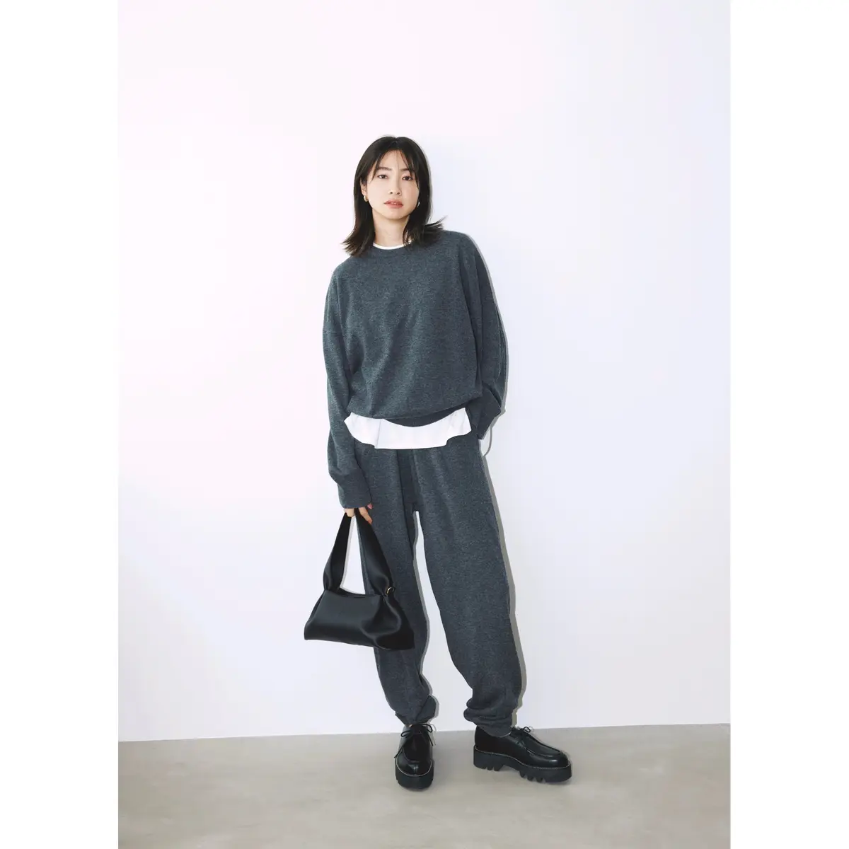 チャコールグレーのクルーネックニットの下に白Tシャツを重ね着し、グレーニットパンツを合わせたコーディネート　モデル・絵美里