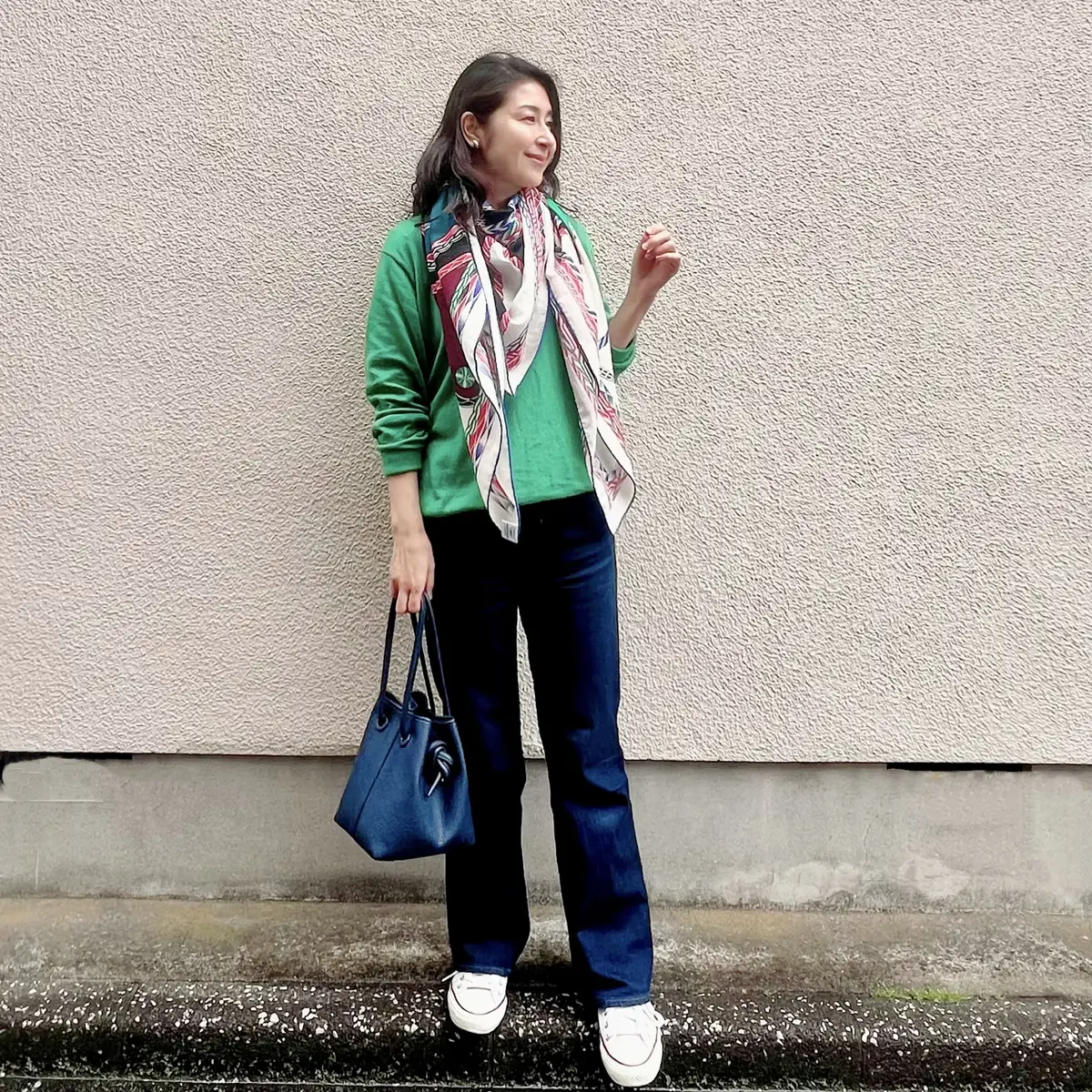 ユニクロ　グリーンのコットンニット、フレアーデニム、大判の柄物ストール、コンバースの白のローカットスニーカー、ネイビーのバッグ