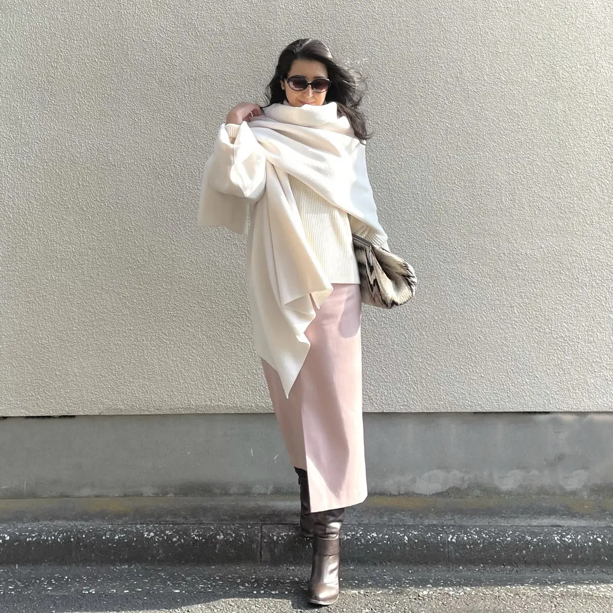 ホワイトの片袖ストール、ホワイトのタートルニット、淡いピンクのタイトスカート、ブラウンのロングブーツ、大きめのクラッチバッグ