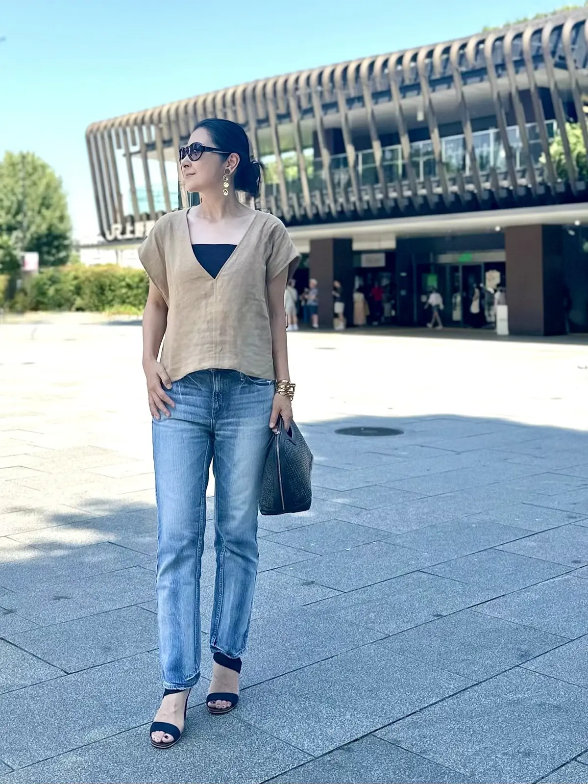 エクラプレミアムのキャメル「リネンコンパクトジレ」、細身のデニム、ネイビーのバッグ、ネイビーのサンダル