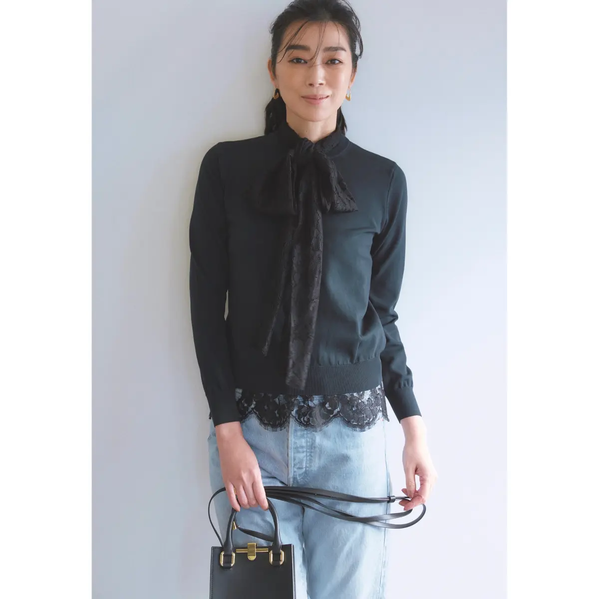 黒レースボウタイブラウスと黒ニットの重ね着に、ライトブルーデニムを合わせたコーデ　モデル・ゆうき