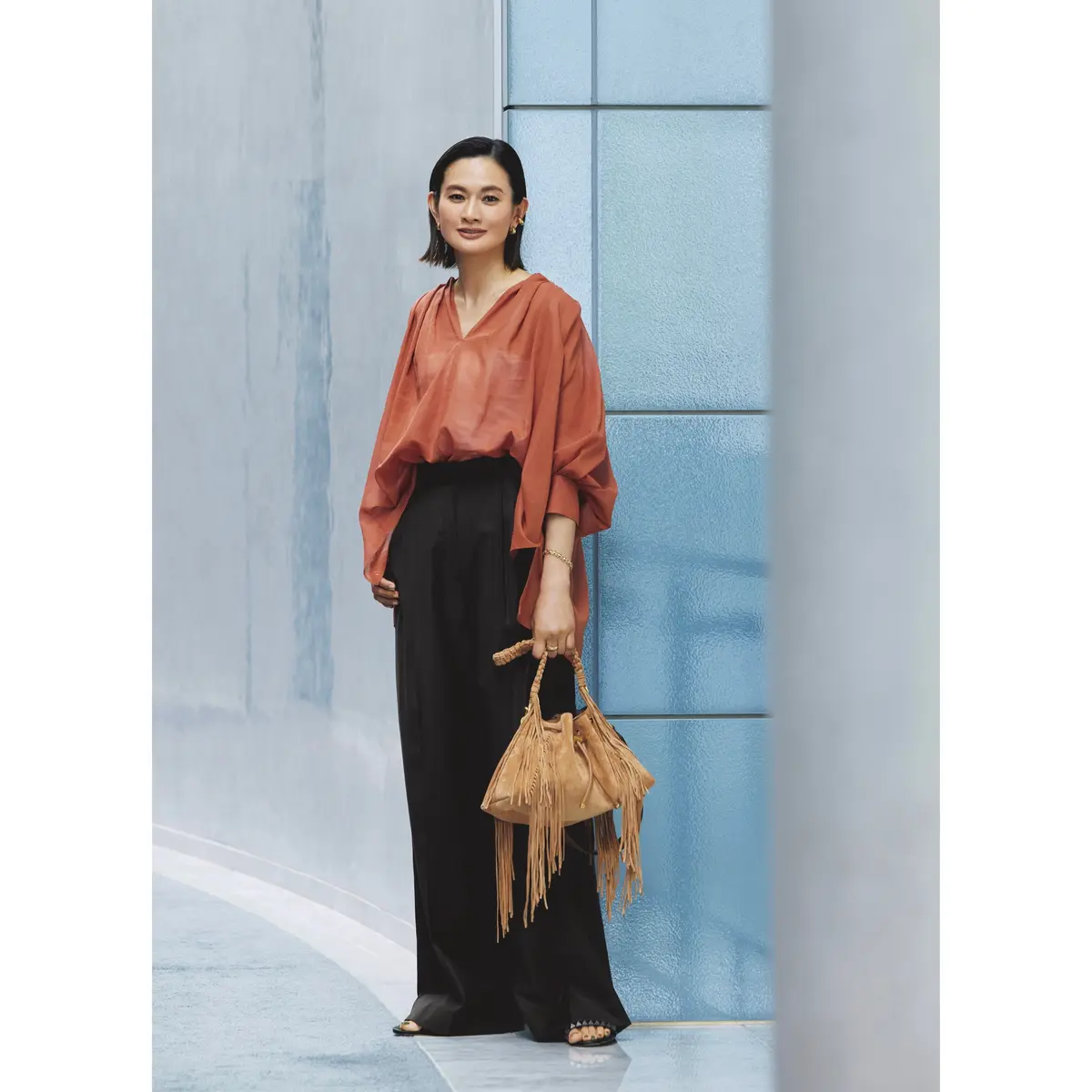 テラコッタカラーのシアーブラウスに黒ワイドパンツを合わせたコーディネート　モデル・渡辺佳子