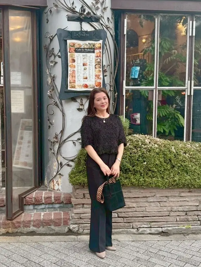 ユニクロのスマートフレアパンツをリピート買い。50代きれいめコーデで新宿御苑ラ・ボエム前に立つ全身写真。黒のフレアパンツにヒールを合わせた大人のランチ会スタイル。