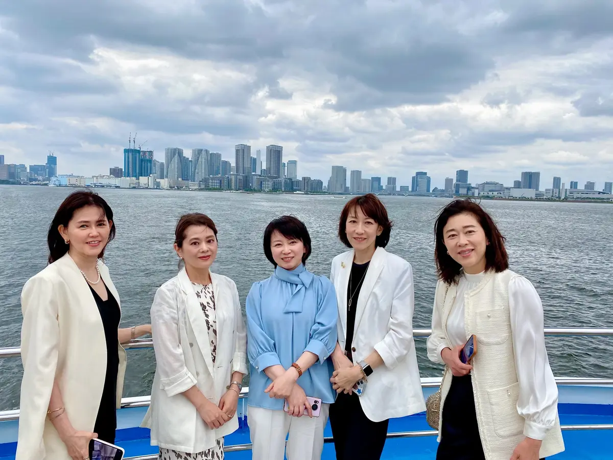 水辺の風景を背に並ぶ5人の女性たち。大人の落ち着いた華やかさが漂う