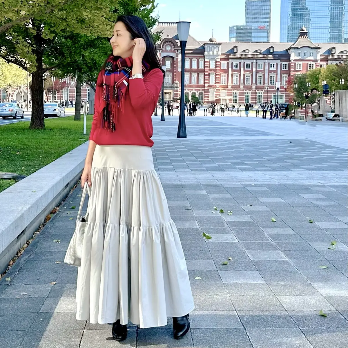 グレーロングスカート、赤ニット、赤のチェック柄ストール、黒ブーツ、シルバーのバッグ